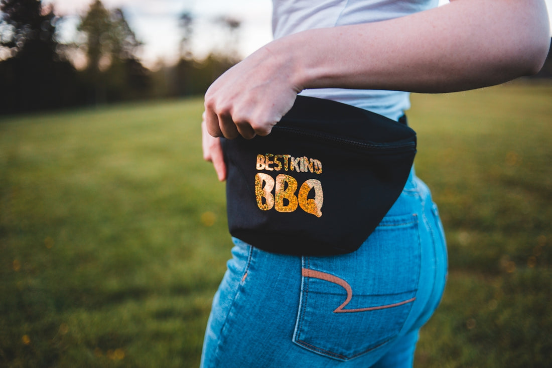 person wearing black and yellow Best Kind BBQ fanny pack standing